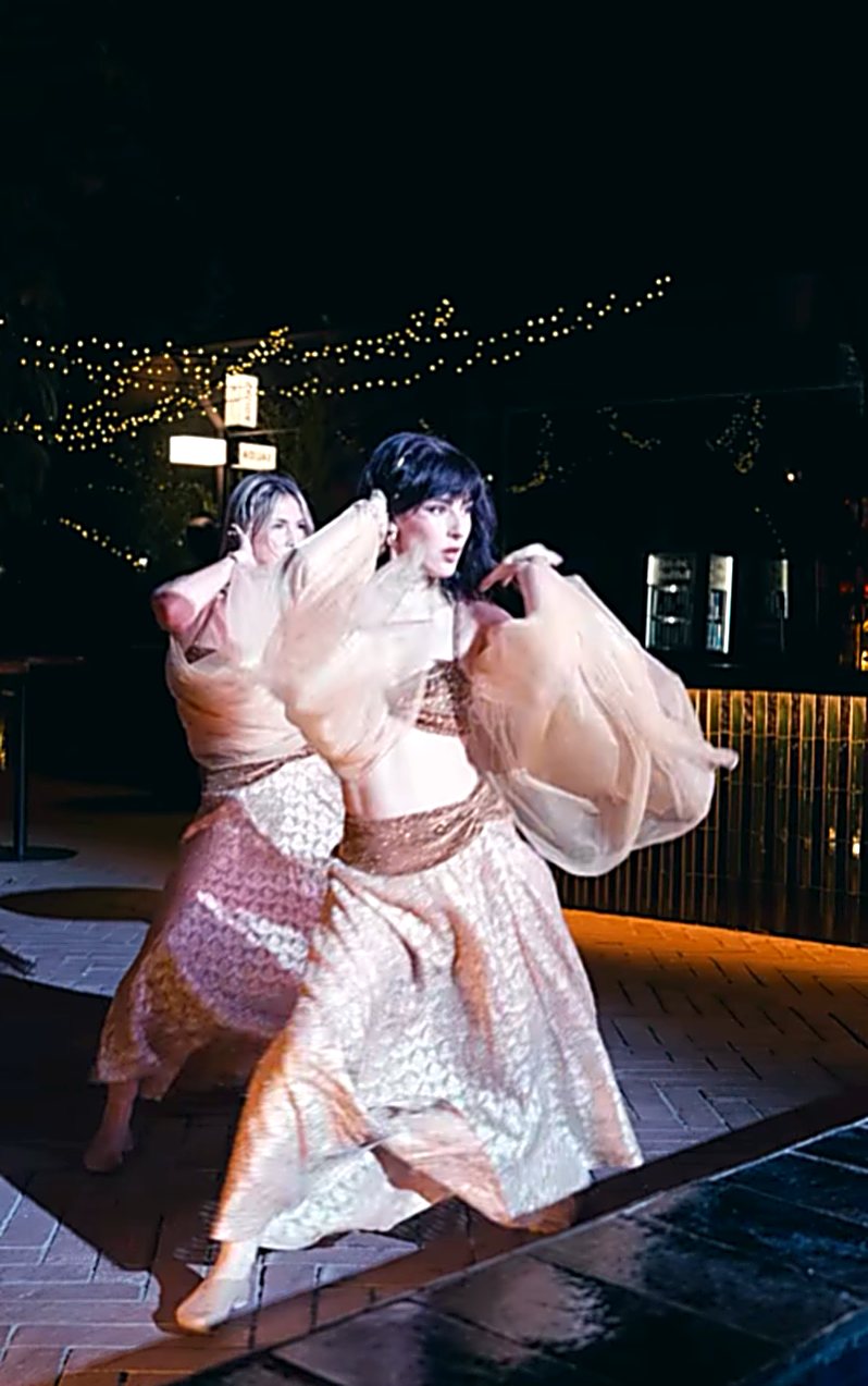 Dos bailarinas con vestuario fluido dorado y rosa en movimiento